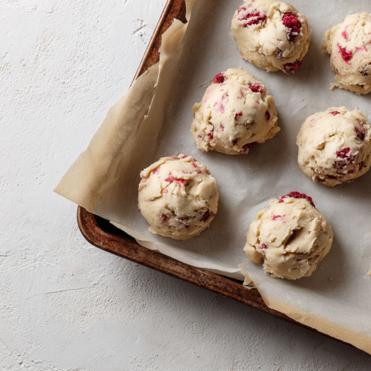 Cookie dough scooped onto a baking tray with raspberries visible

