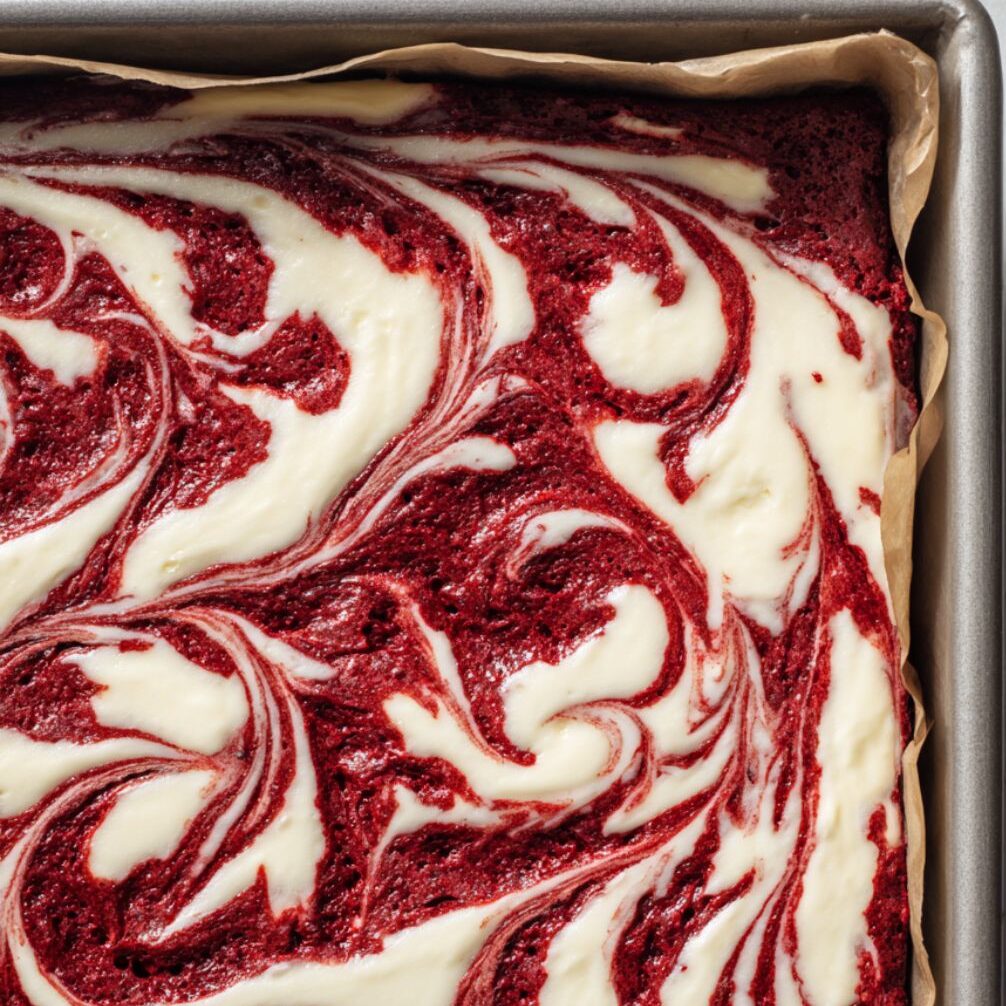 Red velvet brownie batter with cream cheese swirls in a baking pan