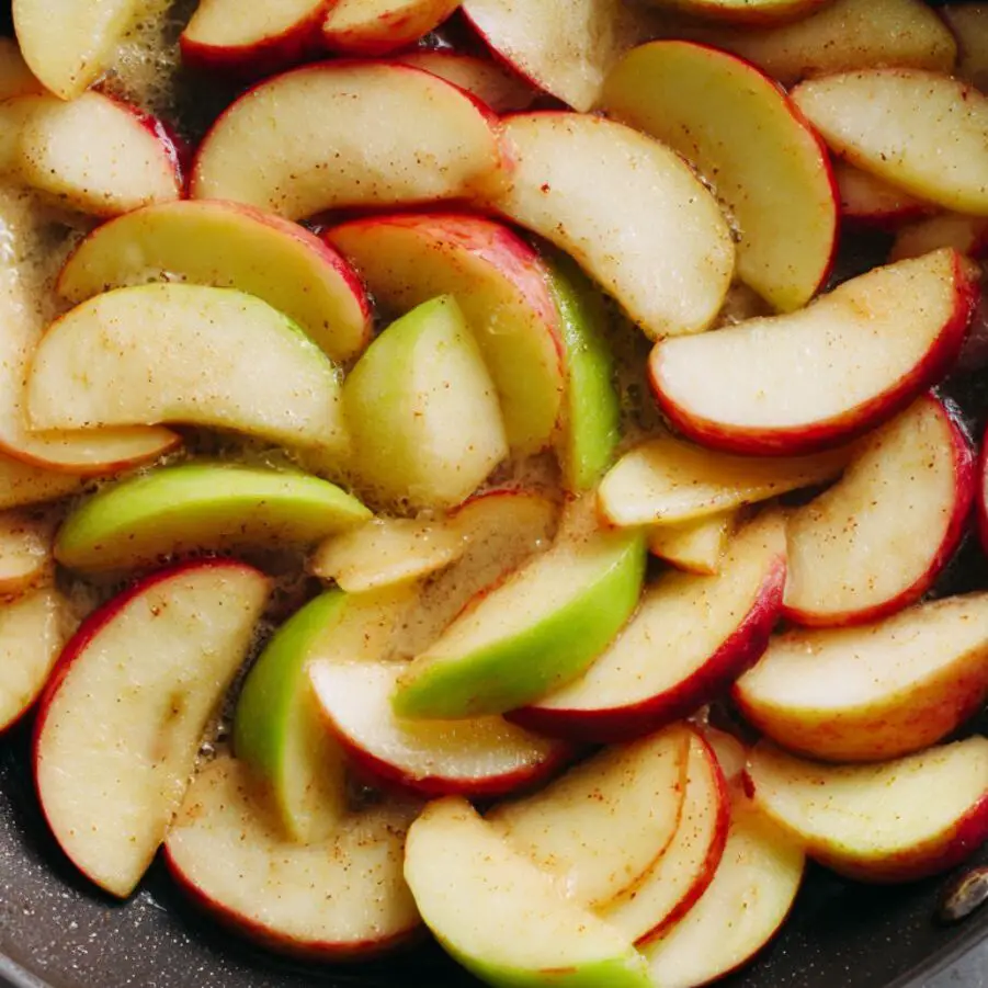 Thin apple slices cooking in butter in a skillet, overhead view.