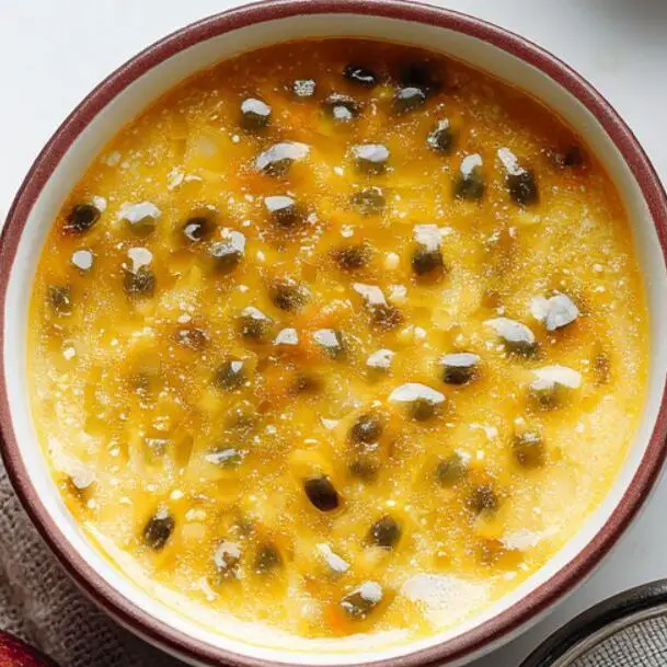 Fresh passion fruit pulp and seeds next to a fine-mesh strainer on a white kitchen counter