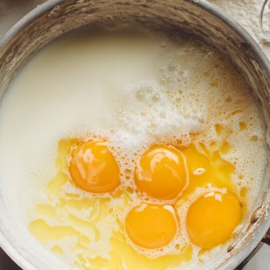 Heating milk and cream and whisking egg mixture for white chocolate pudding

