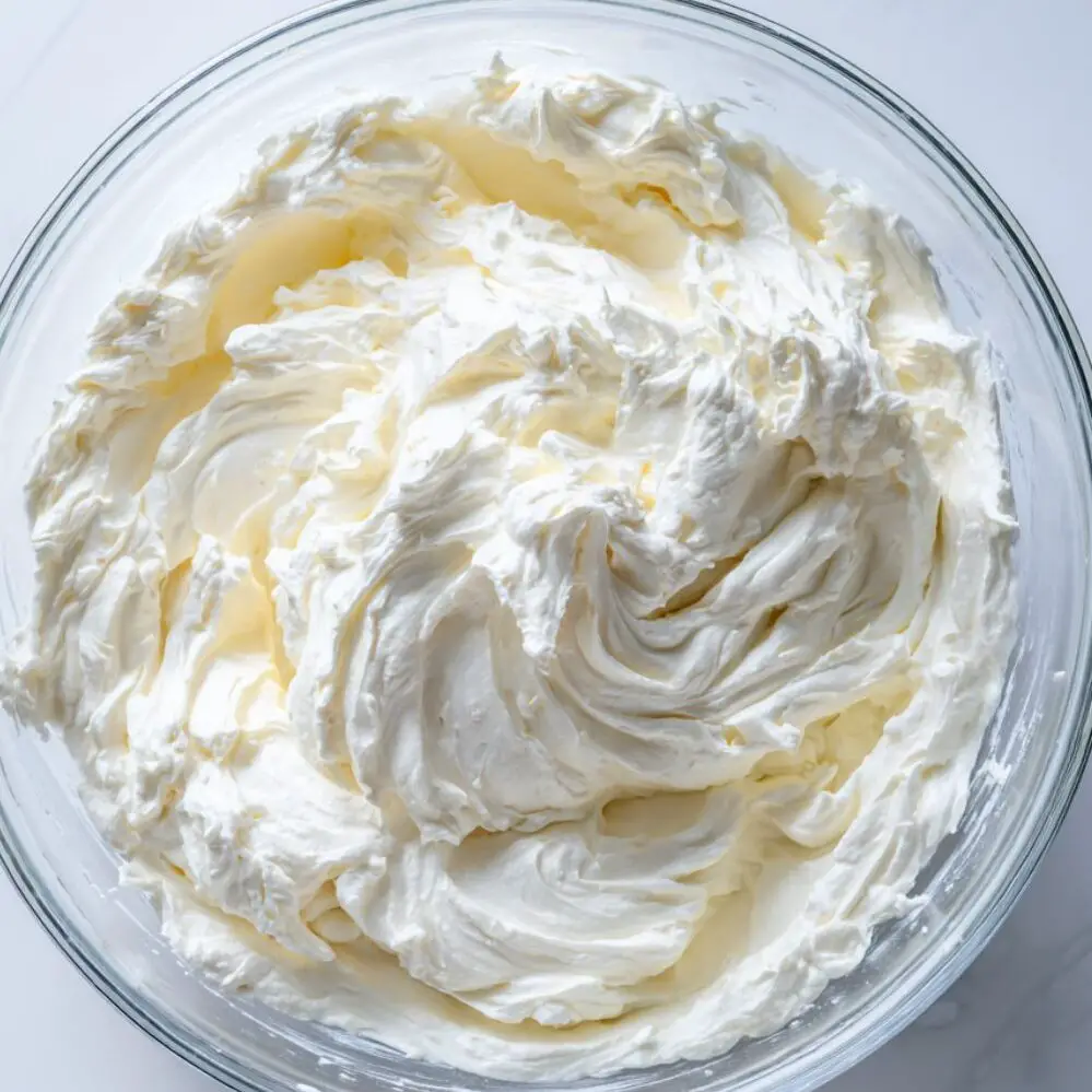 Whipped cream forming soft peaks in a glass bowl.