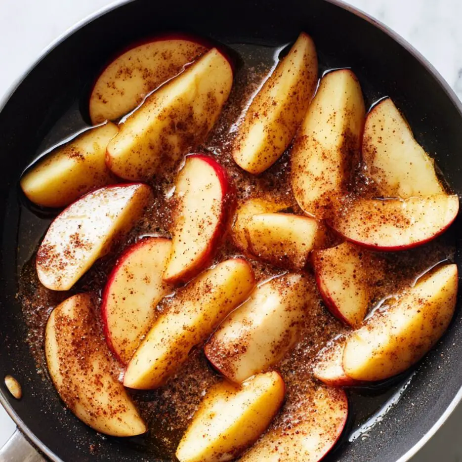 Apple slices caramelizing with cinnamon and sugar in a skillet.