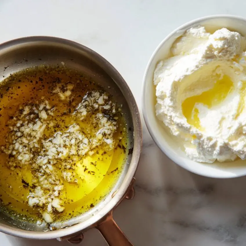 Garlic cooking in olive oil beside ricotta cheese in a pot.