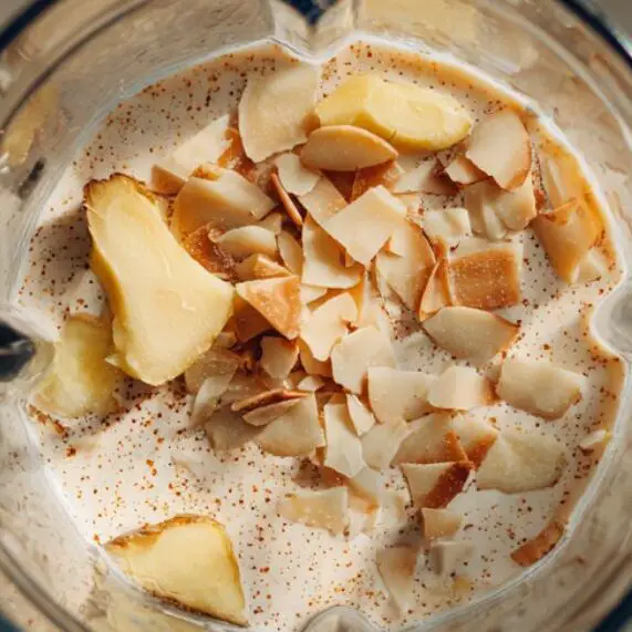 Top view of blender base filled with almond milk, coconut water, and fresh ginger

