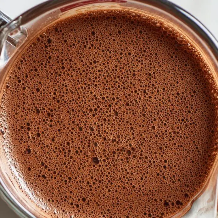 Rich chocolate milk base mixture prepared for bubble tea on a white marble counter.