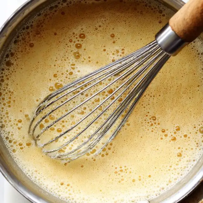 Thickened pudding mixture cooking in saucepan on white counter.

