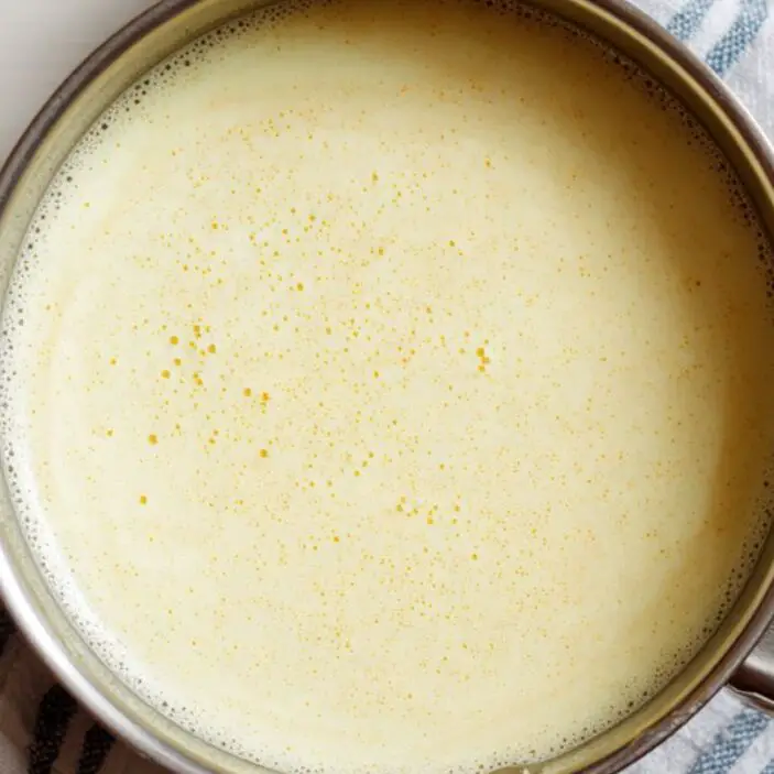 Custard base cooking in a saucepan with a wooden spoon on a white kitchen counter