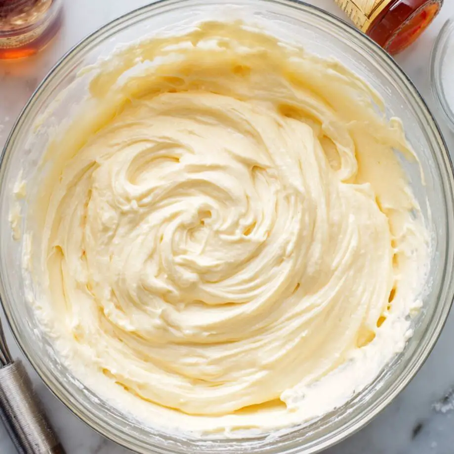 Bowl of creamy ice cream base with whisk and ingredients on counter