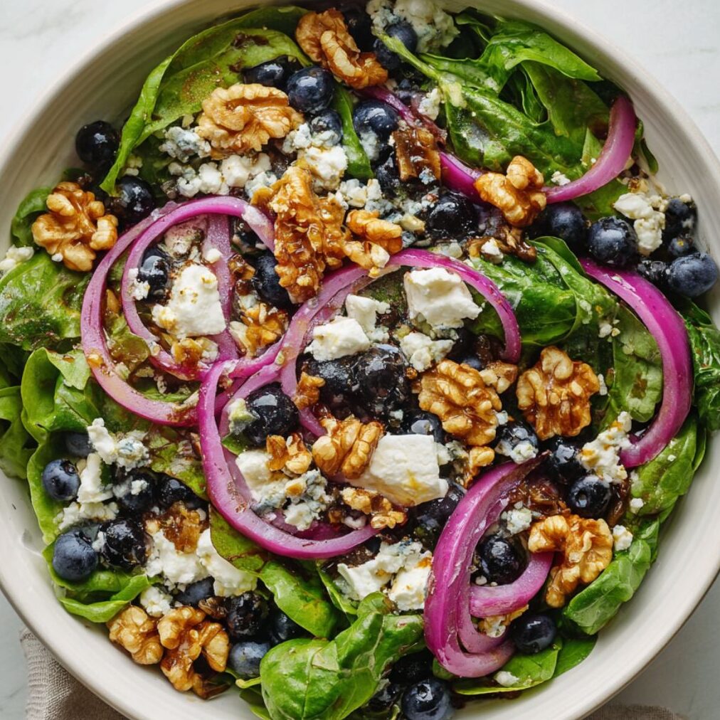 Mixed greens with blueberries, walnuts, onion, and goat cheese in a bowl.