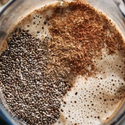 Chia seeds and flaxseed beside an open blender with smoothie base