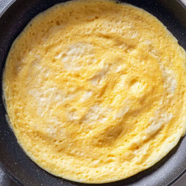 Egg base cooking in a non-stick pan on a white kitchen counter.

