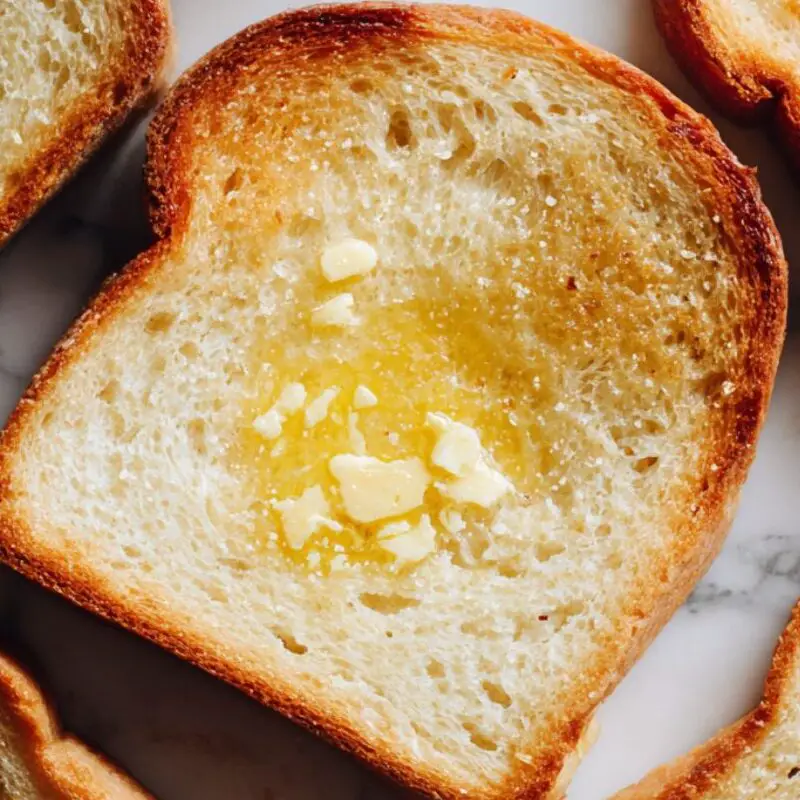 Golden toasted bread slices with butter on a white counter.