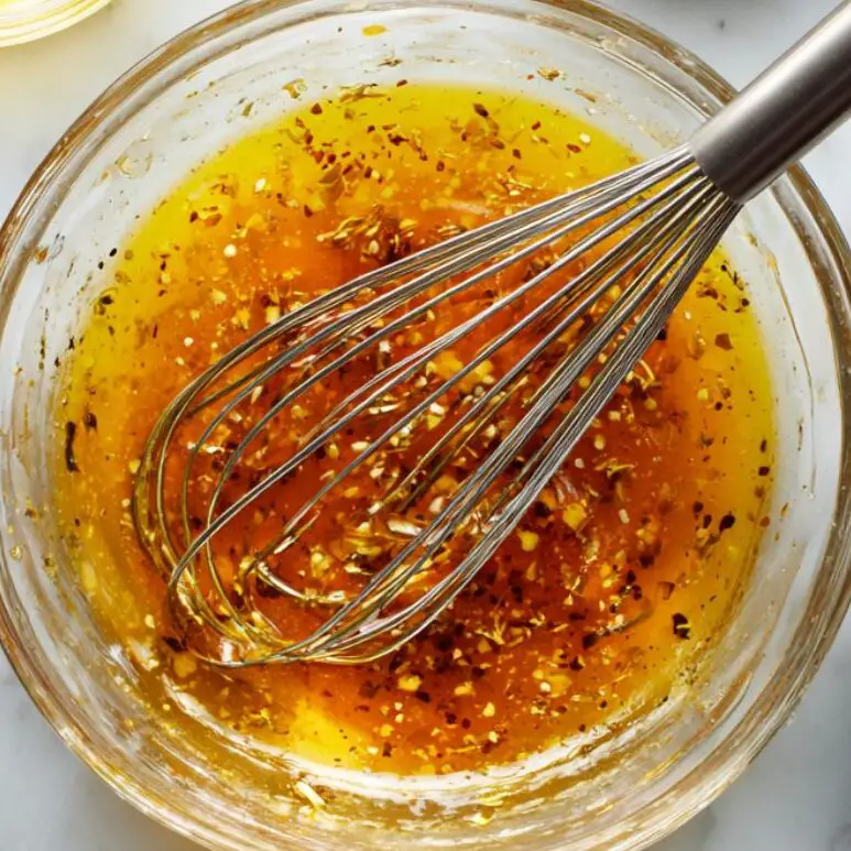 Whisking citrus vinaigrette in a glass bowl with ingredients around