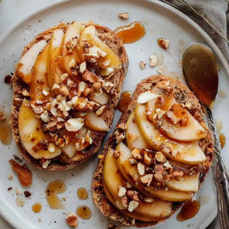 Apple toast topped with caramelized apples and nuts on a white counter.
