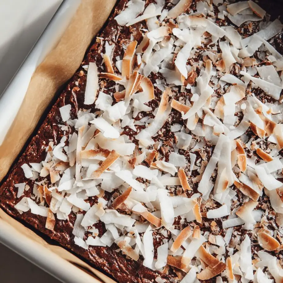 Brownie batter in a lined pan topped with shredded coconut before baking
