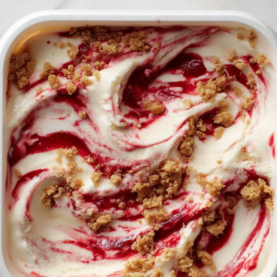 Strawberry cheesecake ice cream swirled with strawberry puree and graham cracker chunks in a freezer container.