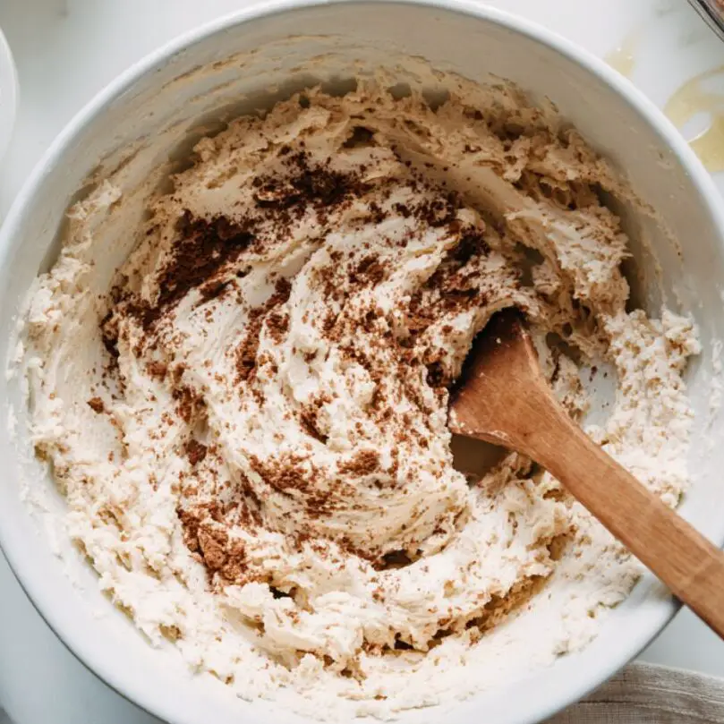 Mixing tiramisu cookie dough in a white bowl on a kitchen counter

