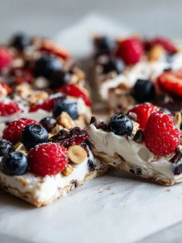 Homemade frozen yogurt bark recipe with berries and granola on parchment paper, broken into rustic pieces, viewed from above on a white kitchen counter