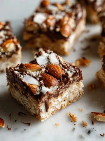 Overhead view of homemade Almond Joy bars recipe cut into rustic squares on a white marble counter with crumbs and chocolate smudges.
