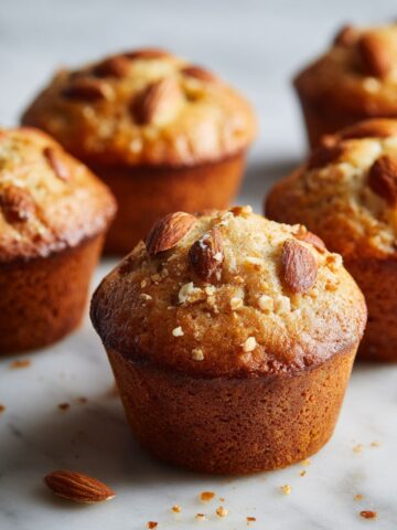 Overhead shot of homemade almond muffins recipe on a white marble kitchen counter with crumbs, rustic and cozy feel.