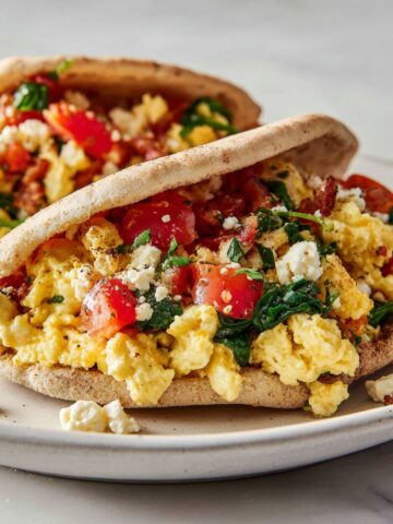 Overhead shot of a homemade breakfast pita recipe stuffed with eggs, tomatoes, spinach, and feta cheese on a white kitchen counter.