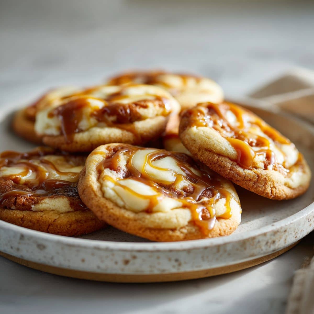 Homemade caramel cheesecake cookies recipe with gooey caramel swirls on a white marble counter, photographed from above.