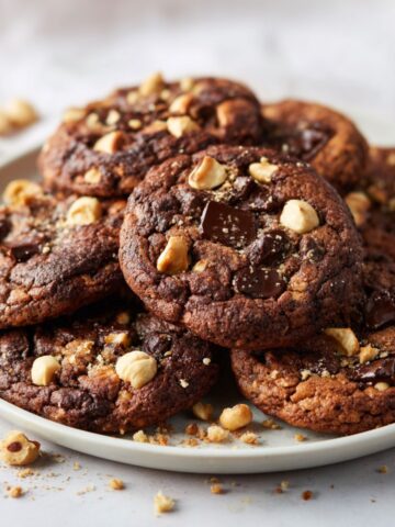 Homemade hazelnut chocolate cookies recipe with gooey chocolate chunks and roasted hazelnuts on a white marble counter, rustic overhead view.