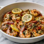 Overhead view of homemade lemon herb shrimp recipe served in a white ceramic pan on a white kitchen counter, garnished with parsley and lemon wedges.