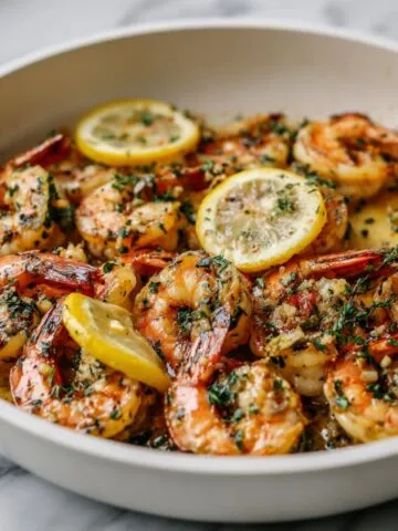 Overhead view of homemade lemon herb shrimp recipe served in a white ceramic pan on a white kitchen counter, garnished with parsley and lemon wedges.