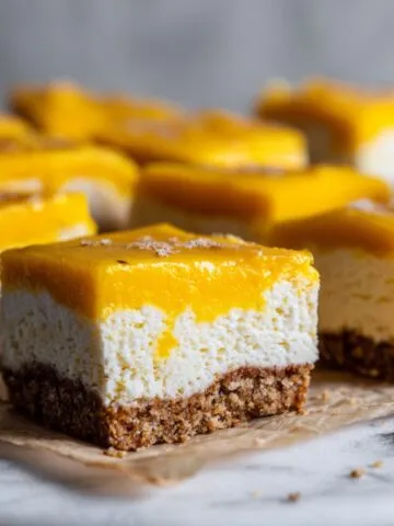 Homemade mango cheesecake bars recipe cut into rustic squares with creamy cheesecake and fresh mango topping on a white kitchen counter.