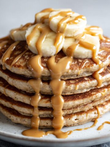 Stack of homemade peanut butter protein pancakes recipe drizzled with peanut butter and banana slices on a white kitchen counter, photographed overhead in a casual homemade style.