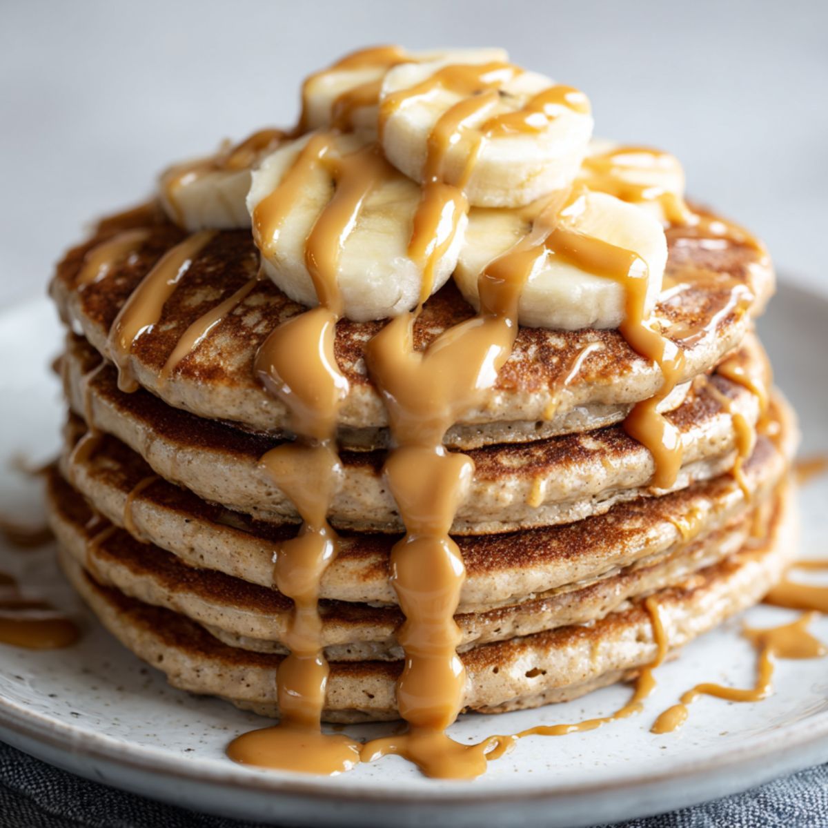 Stack of homemade peanut butter protein pancakes recipe drizzled with peanut butter and banana slices on a white kitchen counter, photographed overhead in a casual homemade style.