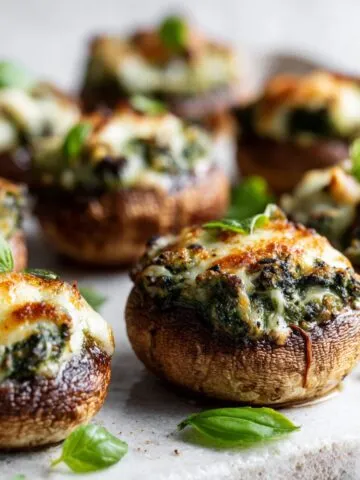 Homemade pesto stuffed mushrooms recipe on a white kitchen counter with melted cheese and basil leaves, photographed from above in natural light.
