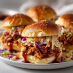 Homemade BBQ jackfruit sliders recipe served on a white counter, topped with coleslaw and BBQ sauce, photographed from overhead.