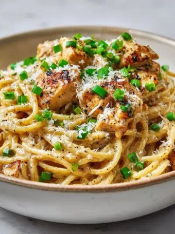 Homemade Cajun chicken spaghetti recipe served in a ceramic bowl on a white kitchen counter, topped with green onions and Parmesan.