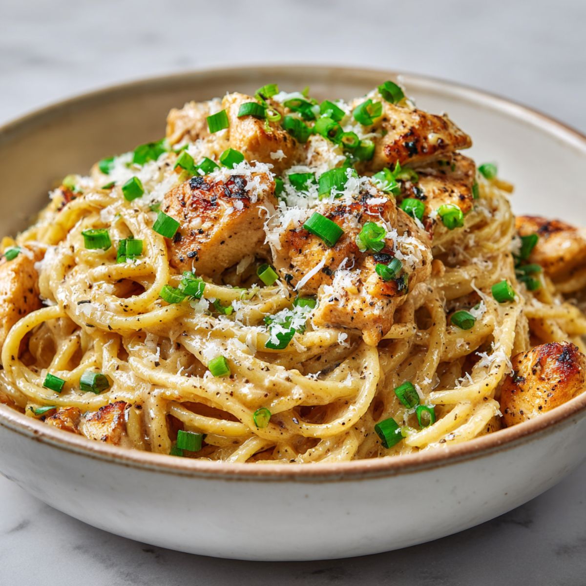 Homemade Cajun chicken spaghetti recipe served in a ceramic bowl on a white kitchen counter, topped with green onions and Parmesan.