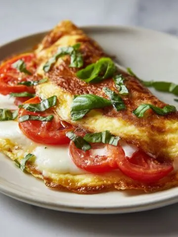 Overhead view of a homemade caprese omelette recipe with mozzarella, tomato, and basil on a white kitchen counter.