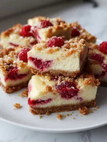 Homemade white chocolate raspberry cheesecake bars recipe cut into squares with rustic raspberry swirls on a white kitchen counter.