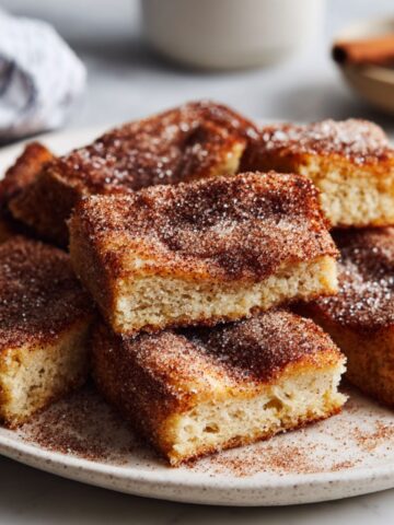 Homemade churro bars recipe dusted with cinnamon sugar on a white kitchen counter, cut into imperfect squares with a rustic, homemade look.