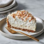 Homemade coconut cream cheesecake recipe on a white counter with a slice pulled out, rustic and natural look.