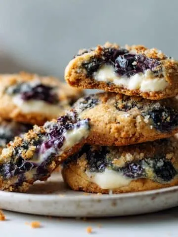 Homemade blueberry cheesecake cookies recipe on a white marble counter, with cheesecake filling and blueberries visible.