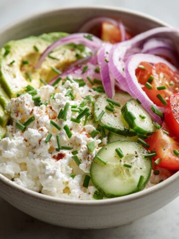 Overhead view of a savory cottage cheese bowl recipe with fresh vegetables and herbs on a white kitchen counter, styled casually for a homemade look.