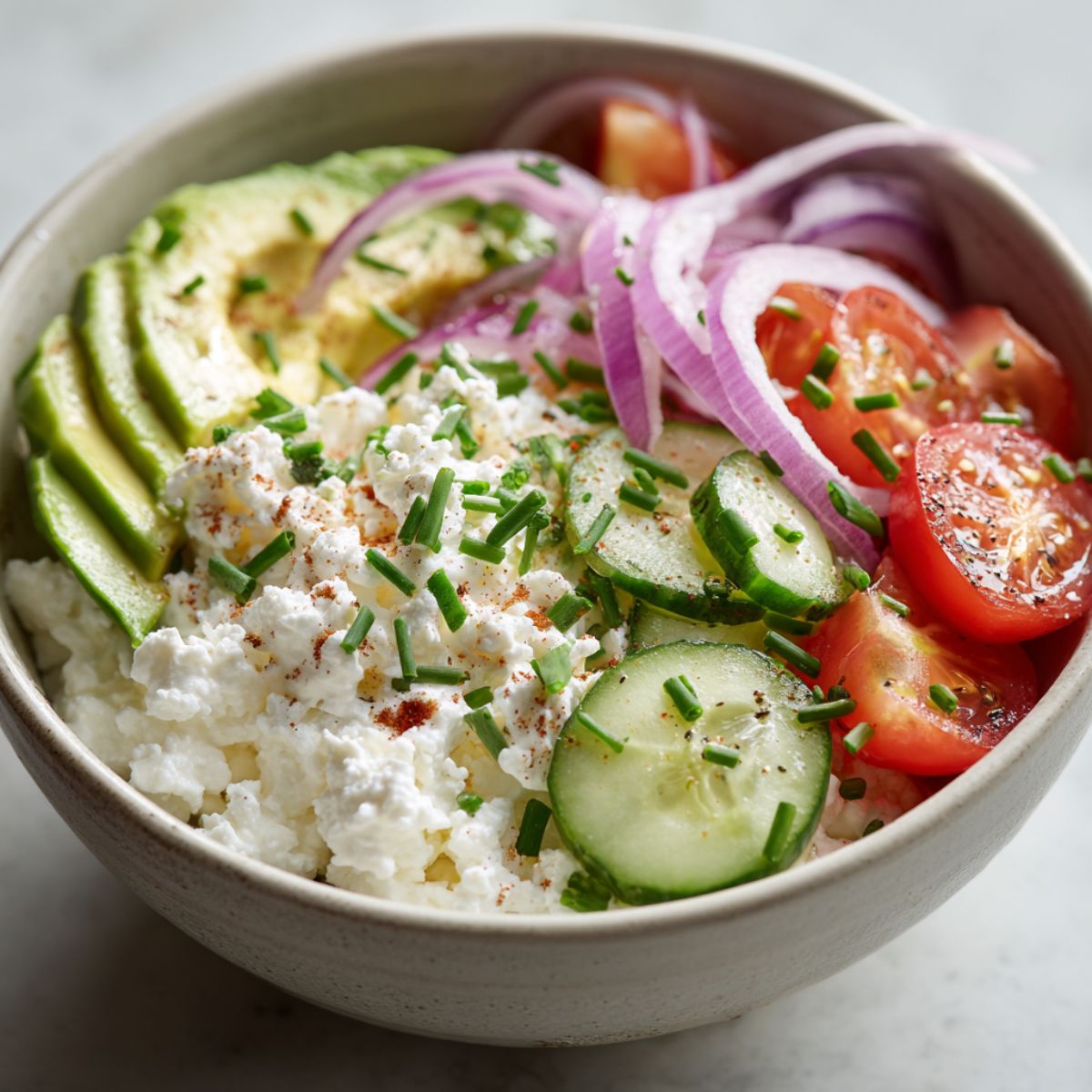 Overhead view of a savory cottage cheese bowl recipe with fresh vegetables and herbs on a white kitchen counter, styled casually for a homemade look.