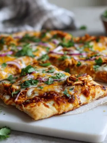 Homemade BBQ chicken flatbread pizza recipe with melted cheese, red onions, and cilantro on a white kitchen counter, photographed from overhead.