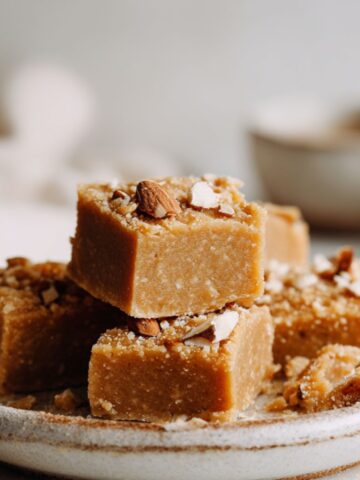 Homemade almond butter fudge recipe squares cut into imperfect pieces on parchment paper on a white kitchen counter.