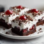 Homemade fudgy Black Forest bars recipe with cherry filling and whipped cream topping on a white marble kitchen counter.