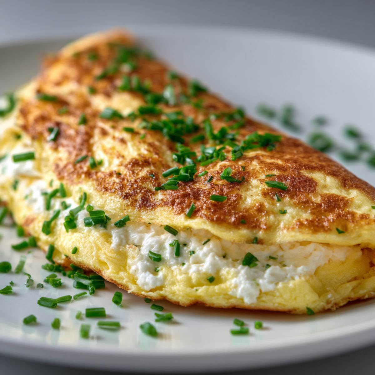 Homemade goat cheese omelette recipe folded with creamy filling and fresh chives, photographed on a white kitchen counter from overhead.