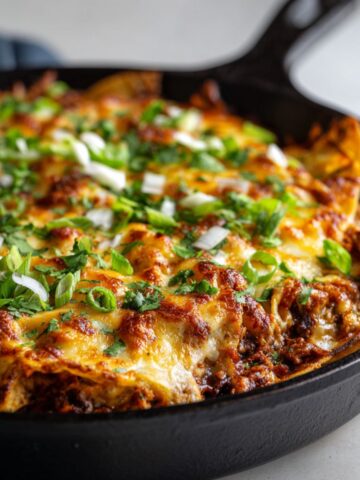Homemade ground turkey enchilada skillet recipe in a cast iron pan with melted cheese, tortilla strips, and fresh cilantro, photographed from overhead on a white kitchen counter.