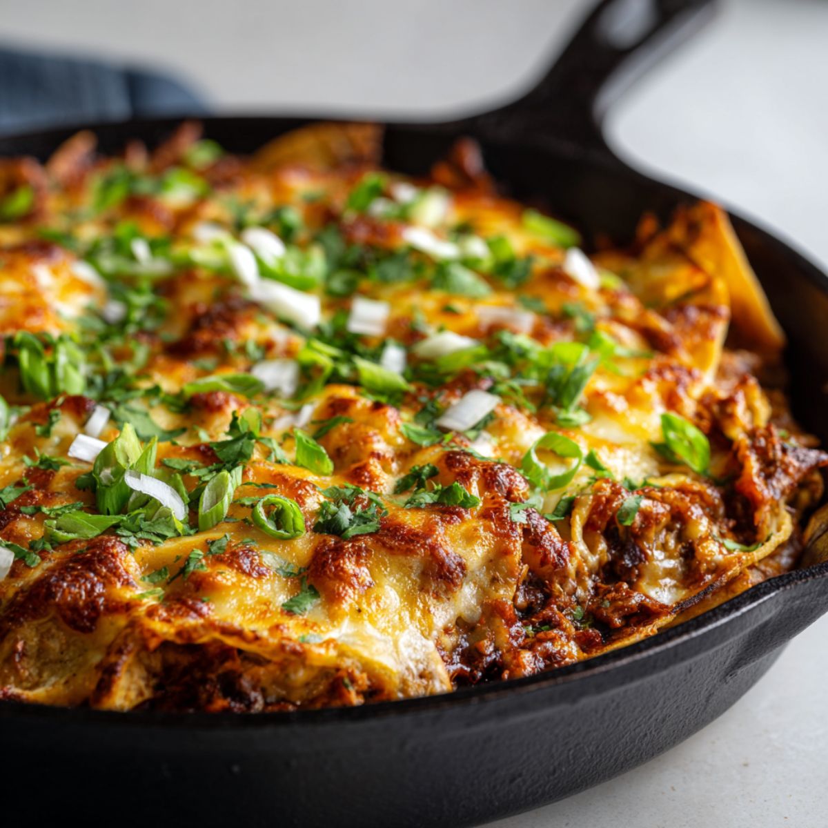 Homemade ground turkey enchilada skillet recipe in a cast iron pan with melted cheese, tortilla strips, and fresh cilantro, photographed from overhead on a white kitchen counter.